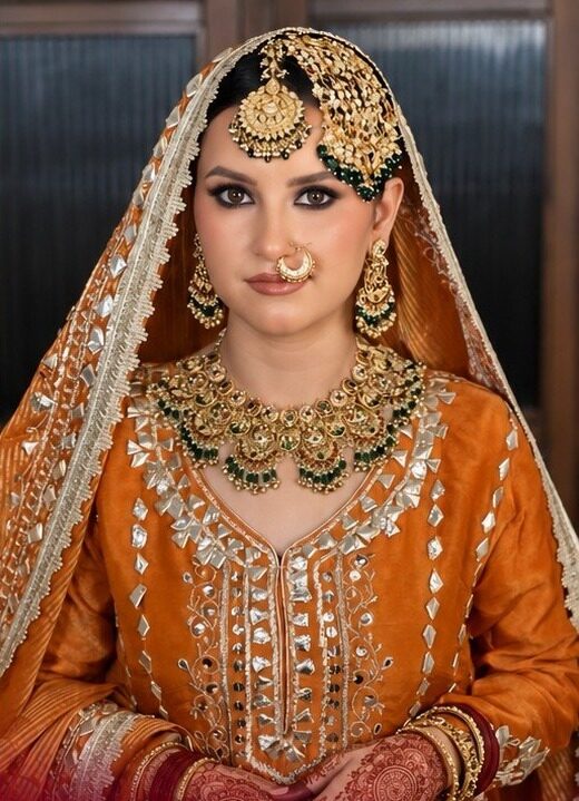 Bride in an orange outfit with a gold dupatta and passa